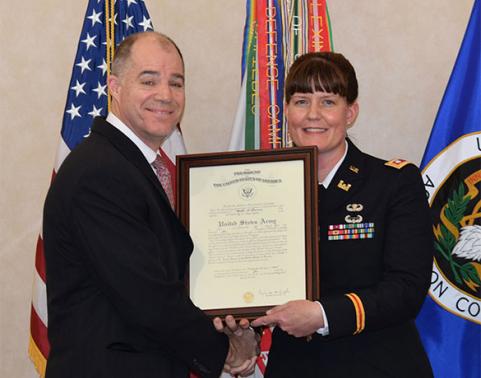 COL Mollie Pearson holds framed charter while shaking hands with man.