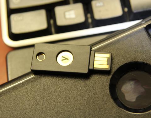 A yubikey authentication token is seen resting on a mobile phone and a computer keyboard.