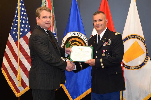 Two men shake hands in front of flags.