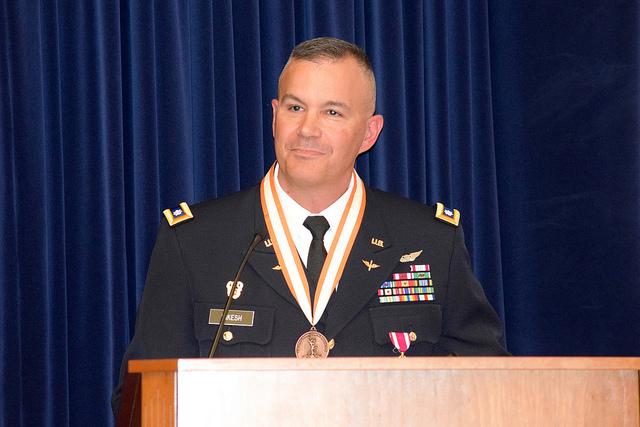 Soldier wearing medal speaks at podium.