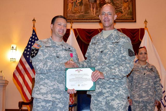 Two soldiers shake hands while both holding a certificate.