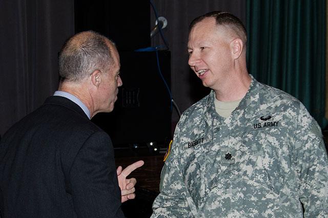 Man on left gestures while talking to a man in a military uniform.