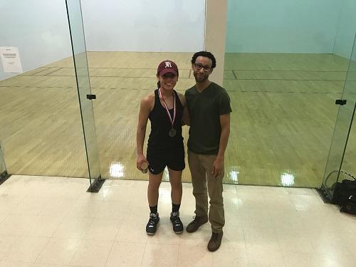Woman and man standing in racquetball court.