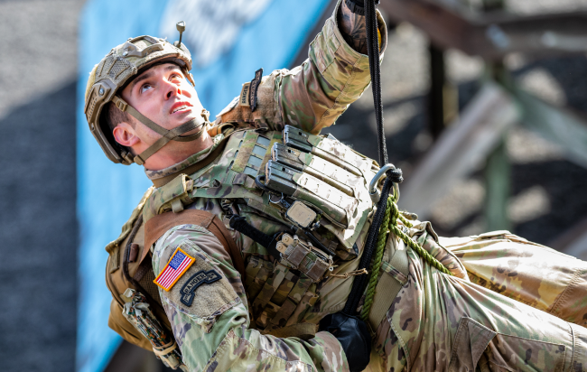 A man dressed in a military uniform repelling down a wall.