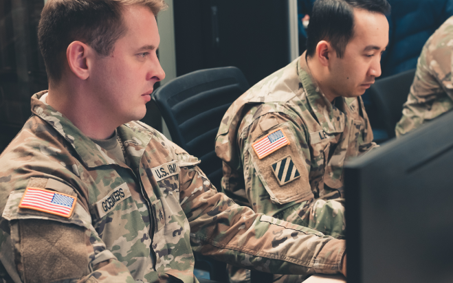 Two men dressed in military uniforms working on computers.